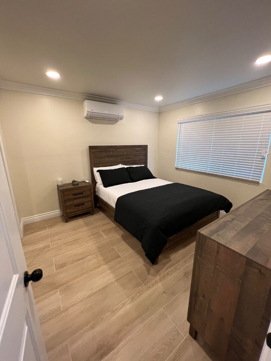 Bedroom with wood bed frame, mirrored closet doors, and mini-split climate control