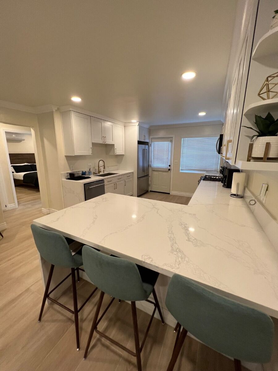 Kitchen island with bar seating, white shaker cabinetry, and view into the living area